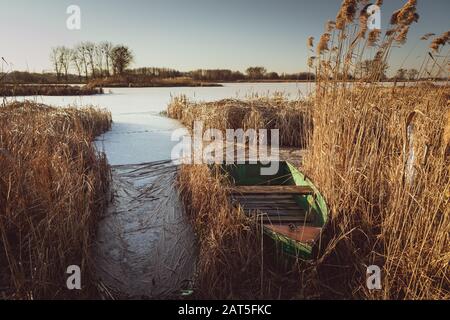 Ein grünes Boot versteckt im Schilf auf einem gefrorenen See Stockfoto