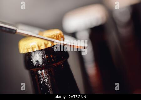 Reihige braune eiskalte Bierflasche mit Wassertropfen und Metallöffnungskappe, dunkler Hintergrund Stockfoto