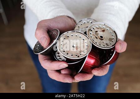 Eine Frau, die eine Handvoll gebrauchte Kaffeepads oder Kapseln aus Aluminium von einer Nespresso-Kaffeemaschine hält. Die Schoten werden recycelt Stockfoto