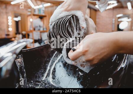 Barber massiert den Kopf des Klientelmanns, wäscht seine Haare mit Shampoo, schwarzem Waschbecken, Vintage-Farbe Stockfoto