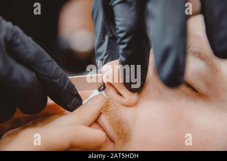 Master barber entfernt Haare aus der Nase des Menschen mit Wachs, Depilation Beauty Verfahren Stockfoto