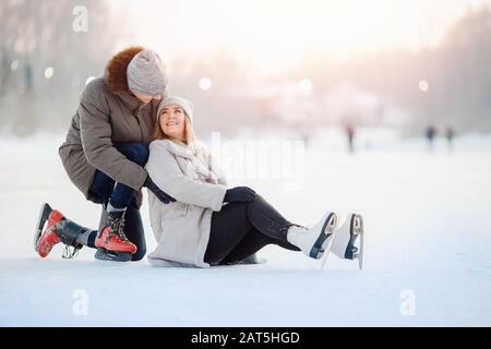 Der Mann hilft Mädchen, auf der Eisbahn aus dem Schnee aufzustehen, und die Winterverletzung fällt. Konzept erste Bekanntschaft, Versicherungszahlung Stockfoto