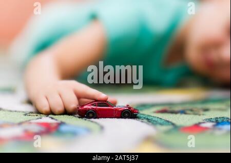 Der Junge rollt ein Spielzeugauto in der Nähe des Bodens. Konzentrieren Sie sich auf Hand und Spielzeug. Stockfoto