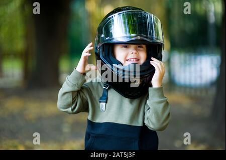 Junge in einem großen Motorradhelm lacht im Herbsttag Stockfoto