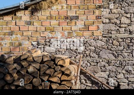 Holzhaufen vor unvollendeter Mauer mit Backsteinen. Holzstämme, Brennstoff zum Heizen. Brennholz aus Holz gestapelt Stockfoto