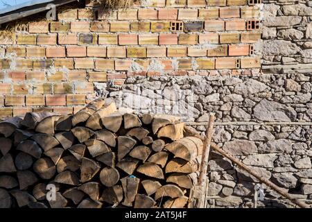 Holzhaufen vor unvollendeter Mauer mit Backsteinen. Holzstämme, Brennstoff zum Heizen. Brennholz aus Holz gestapelt Stockfoto