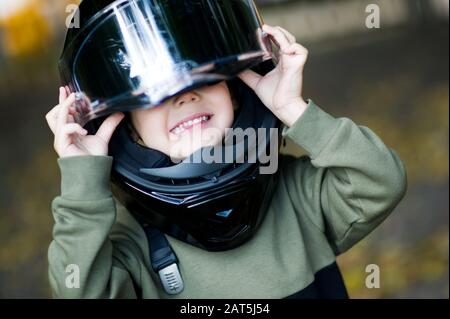 Der Junge ertrank in einem überdimensionierten Motorradhelm, der nicht in seiner Größe ist. Nahaufnahme Stockfoto