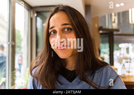 Portrait von Mädchen aus gemischten Rassen, die im Café sitzen und die Kamera betrachten. Mittlere Nahaufnahme. Stockfoto