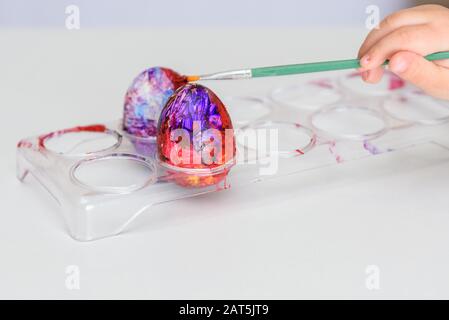 Kind Hände bemalte Ostereier, Farben und Pinsel auf weißer Tisch. Die Vorbereitung auf das Osterfest. Kid Hände zeichnen mit Farben. Stockfoto