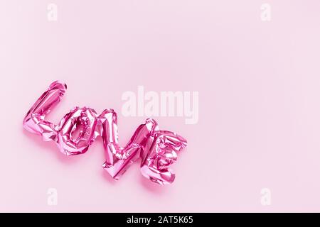 Valentines Tag kreatives Konzept. Aufblasbare pinkfarbene Hochglanzfolie, mit Ballon geformtes Wort Liebe auf pinkfarbenem Hintergrund. Flaches Layout mit Draufsicht und Kopierbereich. Feiertag, Stockfoto