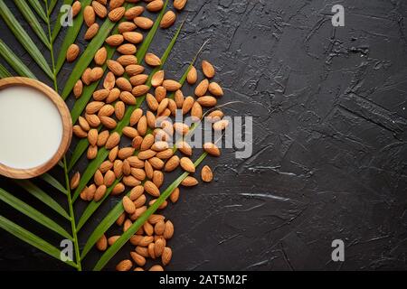 Zusammensetzung von Mandeln, Samen und Milch, auf schwarzem Steingrund. Stockfoto