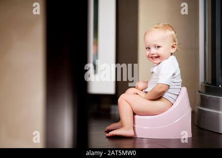 Baby Mädchen sitzt auf einem Topf im Badezimmer und lächelt Stockfoto