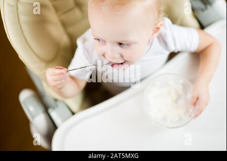 Baby-Mädchen auf einem Babysitz zum Füttern isst Haferbrei, lächelnd fröhlich Stockfoto