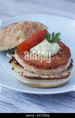 Lachsburger auf einem blauen Teller mit Sauce, Petersilie und Tomatenscheibe öffnen Stockfoto