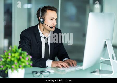 Während der Arbeit an seinem Computer mit Kollegen neben ihm lächelnd Agent Stockfoto