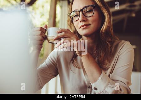 Frau im Café mit einer Tasse Kaffee und Blick auf den Laptop. Geschäftsfrau, die während der Arbeit aus einem Café einen Kaffee hat. Stockfoto