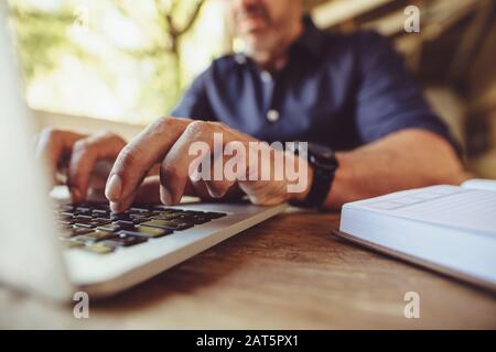 Nahaufnahme des Mannes, der auf seinem Laptop auf dem Tisch in der Café-Bar kesselt. Mann, der seine Arbeit in einem Café macht. Stockfoto