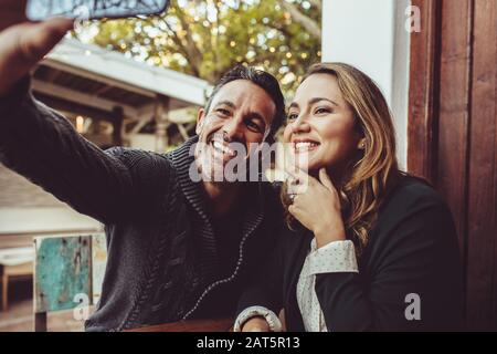 Lächelndes Paar, das im Café sitzt und selfie nimmt. Mann und Frau in der Café-Bar, die mit dem Smartphone ein Selbstporträt machen.