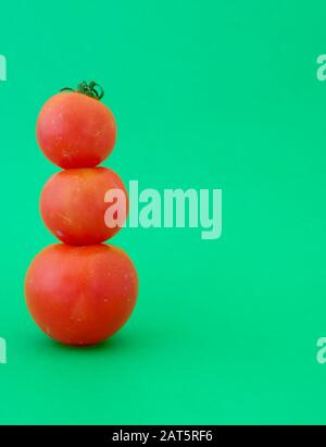 Drei gestapelte rote Tomaten von der größten bis zur kleinsten auf einem hellgrün isolierten Hintergrund Stockfoto