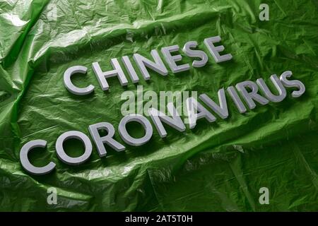 Die Wörter chinesisches Coronavirus wurden mit silbernen Metallbuchstaben auf gelegt Grün zerknitterte Plastikfolie - diagonale Zusammensetzung Stockfoto