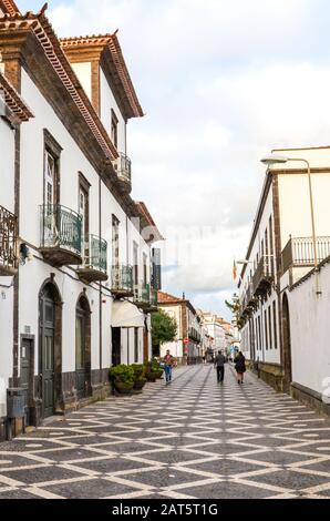 Ponta Delgada, Azoren, Portugal - 12. Januar 2020: Gepflasterte Straße im historischen Zentrum der portugiesischen Stadt. Traditionelle Häuser mit weißen Fassaden. Menschen, die gehen. Vertikales Foto. Stockfoto