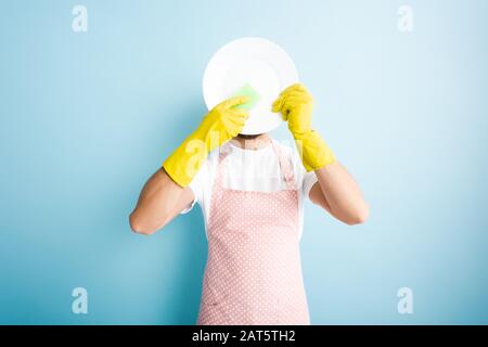 Mann, der den Schwamm in der Nähe der Platte hält und das Gesicht auf dem blauen bedeckt Stockfoto