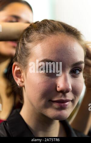 Gesicht der jungen kaukasischen Frau, die die Kamera betrachtet, während sie Haare geflochten hat. Geringe Schärfentiefe. Stockfoto