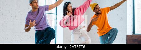 Panoramaaufnahme der jungen Frau und der stilvollen multikulturellen Männer mit Breakdancing Stockfoto