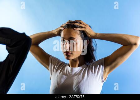 Junge Frau hält die Hände auf dem Kopf. Blauer Hintergrund. Mittlere Nahaufnahme. Wegschauen. Stockfoto