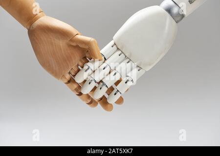 Holzpuppe und Roboterhandschütteln isoliert auf Grau Stockfoto