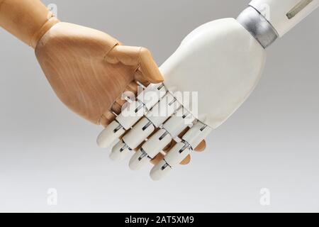 Roboter und Holzpuppe schütteln Hände isoliert auf Grau Stockfoto