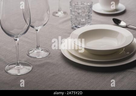 Servieren von Geschirr mit Weingläsern auf grauem Tischtuch Stockfoto