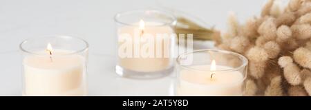 Selektive Fokussierung von flauschigem Bunny-Schwanzrasen und Brennen weißer Kerzen aus Glas, die auf marmorweißer Oberfläche leuchten, Panoramaaufnahme Stockfoto