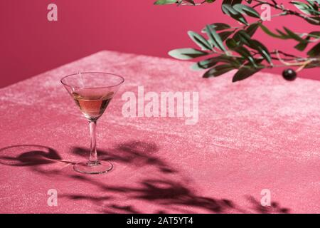 Selektive Fokussierung des Olivenbaumes in der Nähe von Roswein aus Glas auf samtem, pinkfarbenem Tuch, isoliert auf pinkfarbenem, girligen Konzept Stockfoto