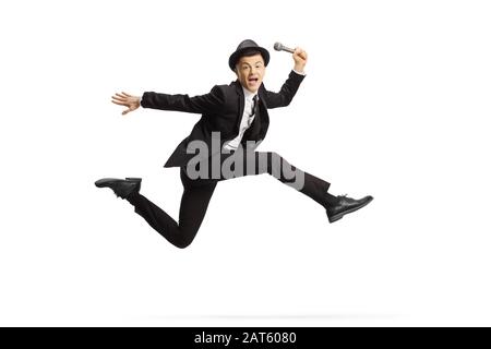 Junger Kerl in einem Anzug, der ein Mikrofon hält und isoliert auf weißem Hintergrund springt Stockfoto