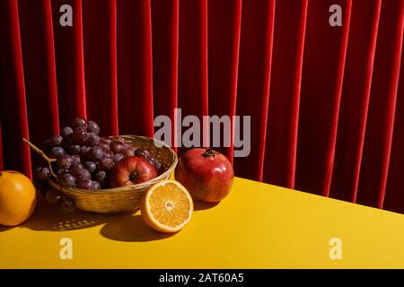 Klassisches Stillleben mit Früchten im Korbkorb auf gelbem Tisch in der Nähe des roten Vorhanges Stockfoto