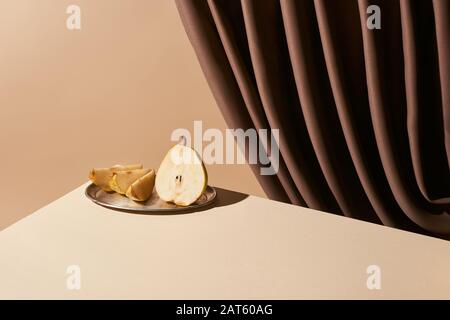 Klassisches Stillleben mit Birne auf silbernem Teller auf Tisch in der Nähe von Vorhang isoliert auf Beige Stockfoto