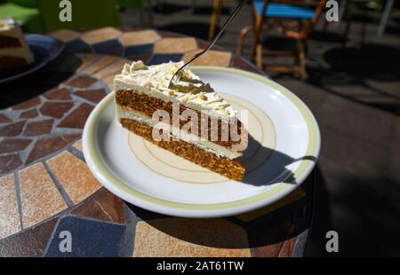 Leckerer Karottkuchen mit einer Gabel, die an einem sonnigen Tag auf einem Teller in einem Café serviert wird. Stockfoto