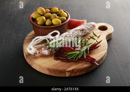 Köstliche Fleischplatte mit Oliven an Bord auf schwarzer Oberfläche Stockfoto