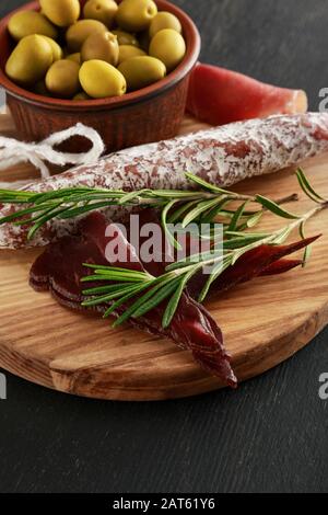Köstliche Fleischplatte mit Oliven an Bord auf schwarzer Oberfläche Stockfoto