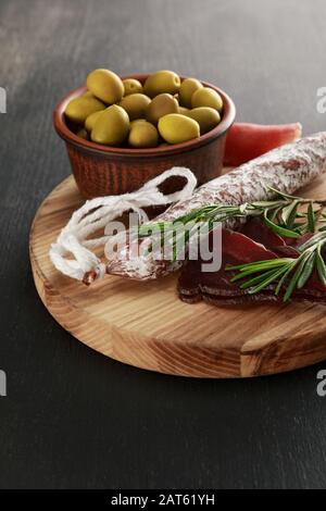Köstliche Fleischplatte mit Oliven an Bord auf schwarzer Oberfläche Stockfoto