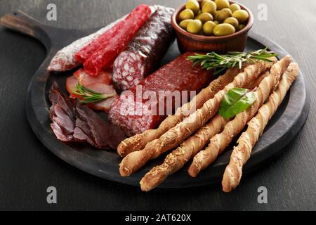 Leckere Fleischplatte mit Oliven und Grissini an Bord auf schwarzer Oberfläche Stockfoto