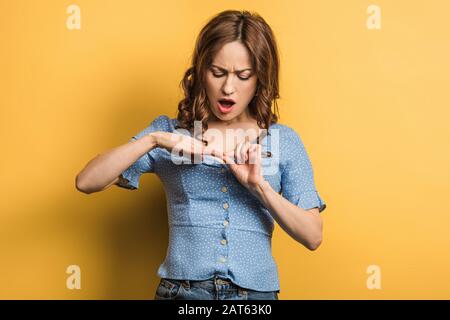 Verärgerte junge Frau, die Nägel auf gelbem Hintergrund berührt Stockfoto
