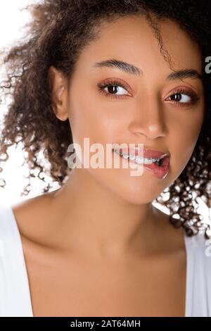 Glückliches afroamerikanisches Mädchen mit Zahnspangen beißender Lippe, isoliert auf Weiß Stockfoto