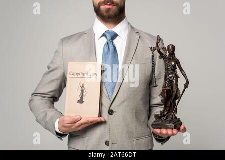 Beschnittener Blick auf den Anwalt, der die themis-statue und das Buch mit dem Titel des Urheberrechts in Grau hält Stockfoto