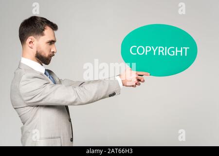 Seitenansicht eines selbstbewussten Geschäftsmannes, der Sprechblase mit einem auf Grau isolierten Wort-Copyright hält Stockfoto