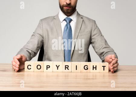 Beschnittenes Bild von Geschäftsleuten, die am Schreibtisch in der Nähe von Holzwürfeln sitzen, mit Wort Copyright isoliert auf Grau