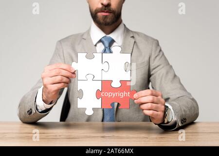 Beschnittener Blick auf Unternehmer, die Puzzle mit Wort Copyright auf grau isoliert halten Stockfoto