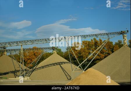 Mehrere Schotterhaufen aus einer Schotteranlage vor herbstlichem Hintergrund in Deutschland mit Förderbändern Stockfoto