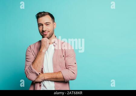 Fröhlicher, gutaussehender Mann, der denkt und die Kamera betrachtet, isoliert auf Blau Stockfoto